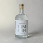 Clear gin bottle with gold cap on a light gray background