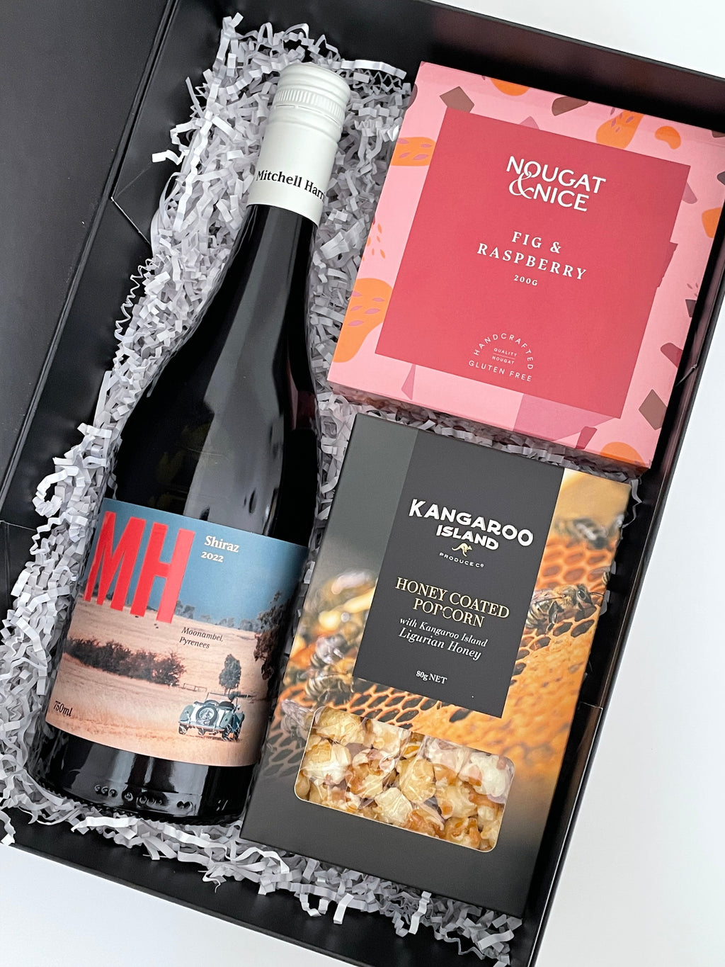 MH Shiraz Wine bottle with fig and raspberry nougat and honey coated popcorn in a gift box on a white background